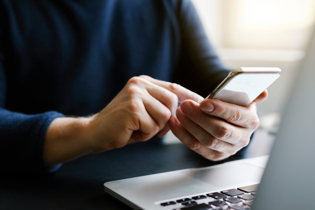 Person using a mobile phone in front of a laptop.